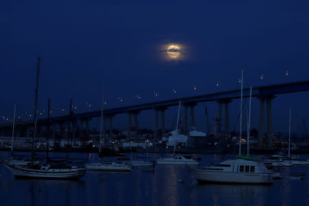 A full moon rises between clouds and above the Coronado Bridge before the start of a total lunar eclipse that is called a 'Super Blood Wolf Moon' in San Diego, California, U.S., January 20, 2019. REUTERS/Mike Blake