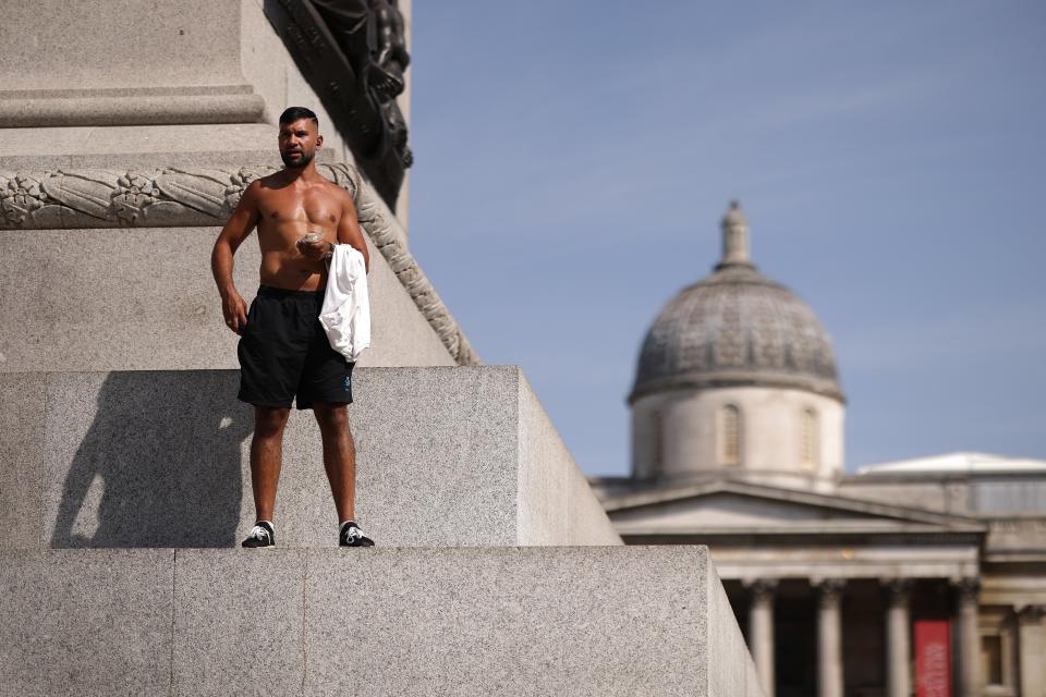 A man holds his top as he stands in the heat on the side of one of the plinths in Trafalgar Square (Getty Images)