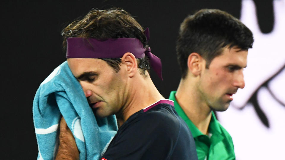 Roger Federer wipes his face with a towel as he passes Novak Djokovic.