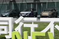 A woman walks past cars by Volkswagen a day before the auto show in Beijing, Wednesday, April 24, 2024. Foreign automakers have been caught flat-footed in China by an electric vehicle boom that has shaken up the market over the last three years. That has left manufacturers like Volkswagen scrambling to develop new models for a very different market than at home. (AP Photo/Ng Han Guan)