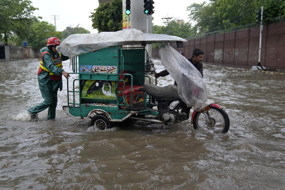 A rescue worker helps a driver pushing his motorcycle rickshaw through a flooded road caused by heavy monsoon rainfall in Lahore, Pakistan, Wednesday, July 5, 2023. Officials say heavy monsoon rains have lashed across Pakistan, killing a number of people. (AP Photo/K.M. Chaudary)