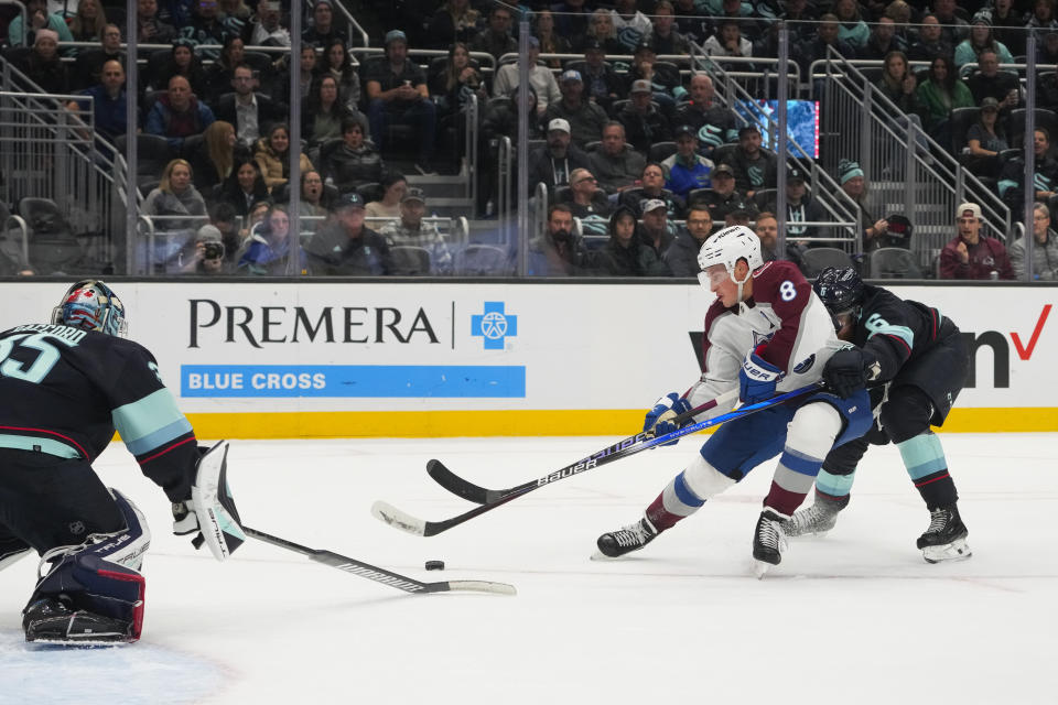 Colorado Avalanche defenseman Cale Makar (8) looks to shoot against Seattle Kraken goaltender Joey Daccord, left, while being pursued by Kraken defenseman Adam Larsson (6) during the second period of an NHL hockey game, Monday, Nov. 13, 2023, in Seattle. (AP Photo/Lindsey Wasson)