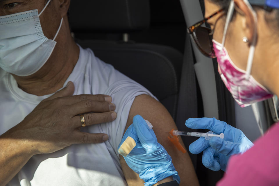 A health care worker administers an injection to someone sitting in a car.