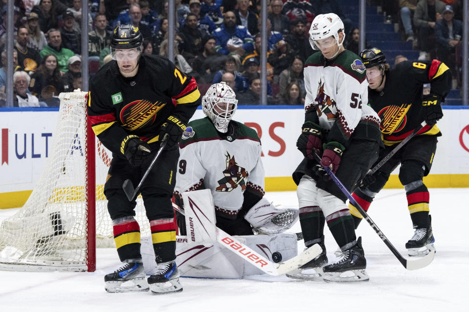 Arizona Coyotes goaltender Connor Ingram (39) stops the puck as Vancouver Canucks' Nils Hoglander (21) and Brock Boeser (6) and Coyotes' Vladislav Kolyachonok (52) watch during the third period of an NHL hockey game Wednesday, April 10, 2024, in Vancouver, British Columbia. (Ethan Cairns/The Canadian Press via AP)