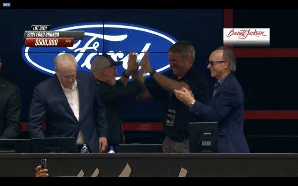 The Rev. Tim McCabe, executive director of Pope Francis Center, left, high-fives Henry Ford III on stage at the Barrett-Jackson auction on Thursday in Scottsdale, Arizona. The event raised $500,000 for the charity with the sale of a custom 2021 First Edition Ford Bronco.