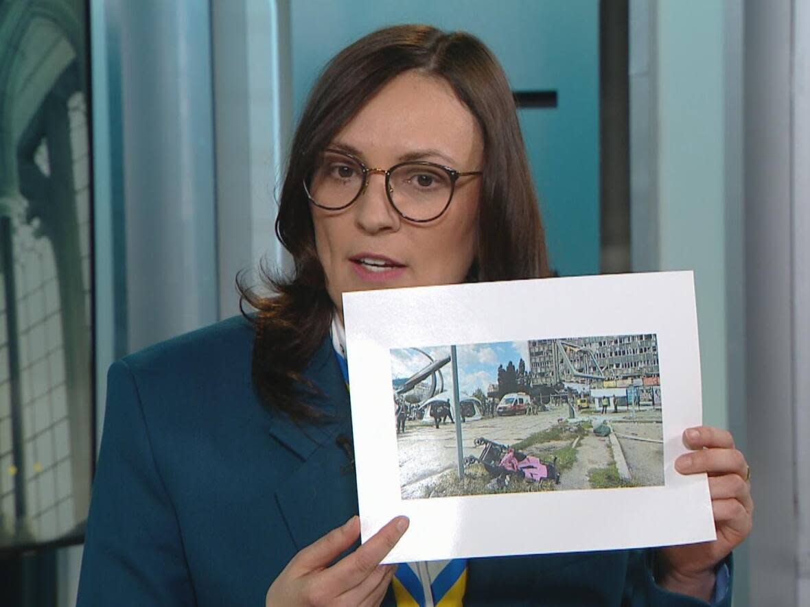 Yuliya Kovaliv, Ukraine's ambassador to Canada, held up this photo of the scene following the death of a child in a Russian Kalibr missile strike in 2022 that shows emergency crews in the background of an overturned stroller.  (CBC News - image credit)