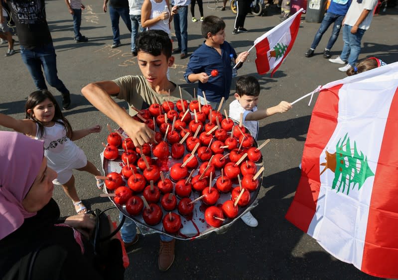 Children hold the national flag as a boy sells caramel apples during an anti-government protest in the port city of Sidon