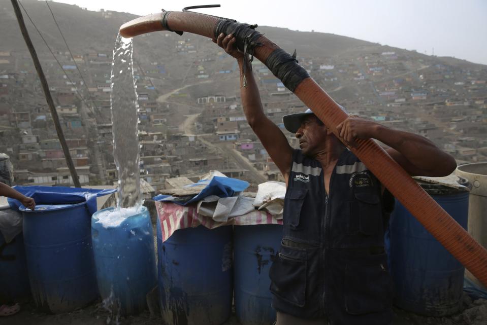 Un trabajador de camión cisterna llena un contenedor con agua por el costo aproximado de 1.5 dólares por contenedor afuera de las casas de residentes que usan el líquido para beber, cocinar y limpiar en el barrio de Nueva Esperanza en Lima, Perú, el jueves 21 de marzo de 2019. (AP Foto/Martin Mejia)