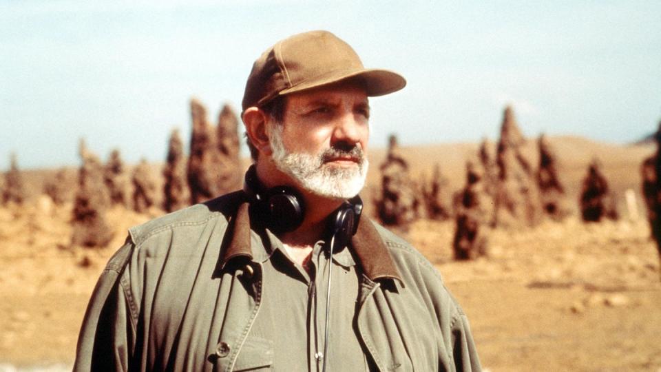 a man wearing a hat and a microphone in front of a desert