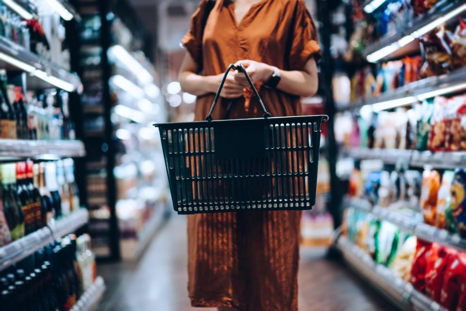 Woman standing in a grocery aisle with an empty basket