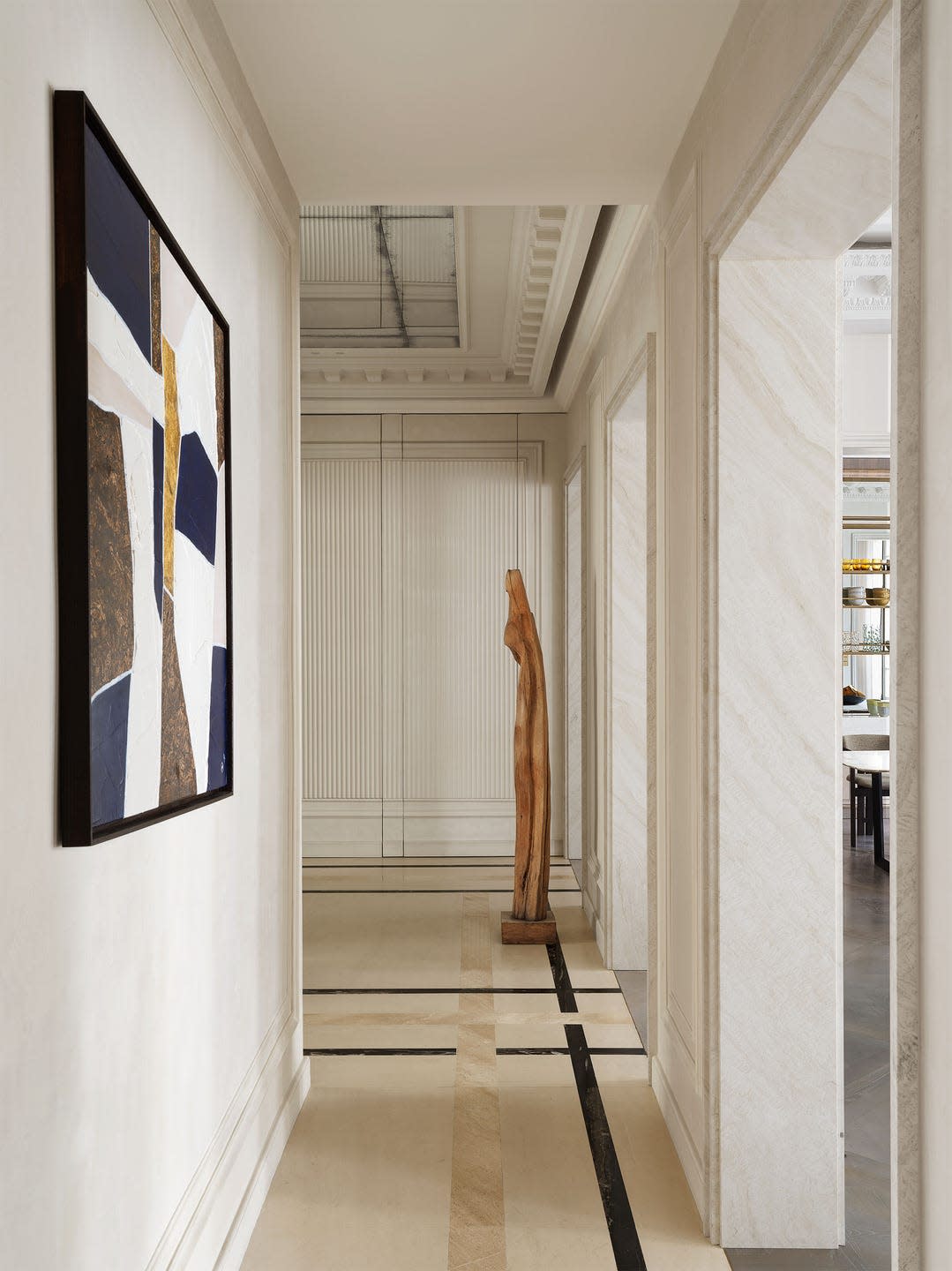 hallway with light colored walls, marble floor with different color insets, framed artwork and left wall, human size wood sculpture, fluted wall treatment