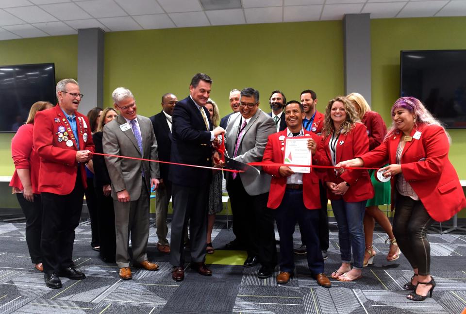 Jim Springfield, president of Blue Cross and Blue Shield of Texas (left, holding scissors) prepares to cut a ceremonial ribbon with Michael Garcia, senior director of customer service for the Abilene office, with members of the Abilene Chamber of Commerce Redcoats May 17.
