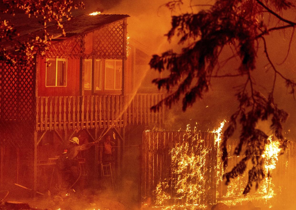 Firefighters work to save a home as the Dixie Fire tears through the Indian Falls community in Plumas County, Calif. on Saturday, July 24, 2021. The home, along with neighboring residences, ended up burning.