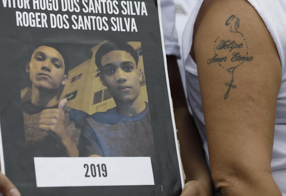 A demonstrator holds a photo of youths who were killed during a police operation, next to a woman with the tattooed words: "Felipe, Eternal Love," referring to a dead relative, during a protest against police violence in poor "favela" neighborhoods, on Ipanema beach in Rio de Janeiro, Brazil, Sunday, May 26, 2019. According to police, the youths at left were killed during an exchange of gunfire, while family members and neighbors say they were executed by police. The woman at right said Felipe was killed during a police operation. (AP Photo/Silvia Izquierdo)