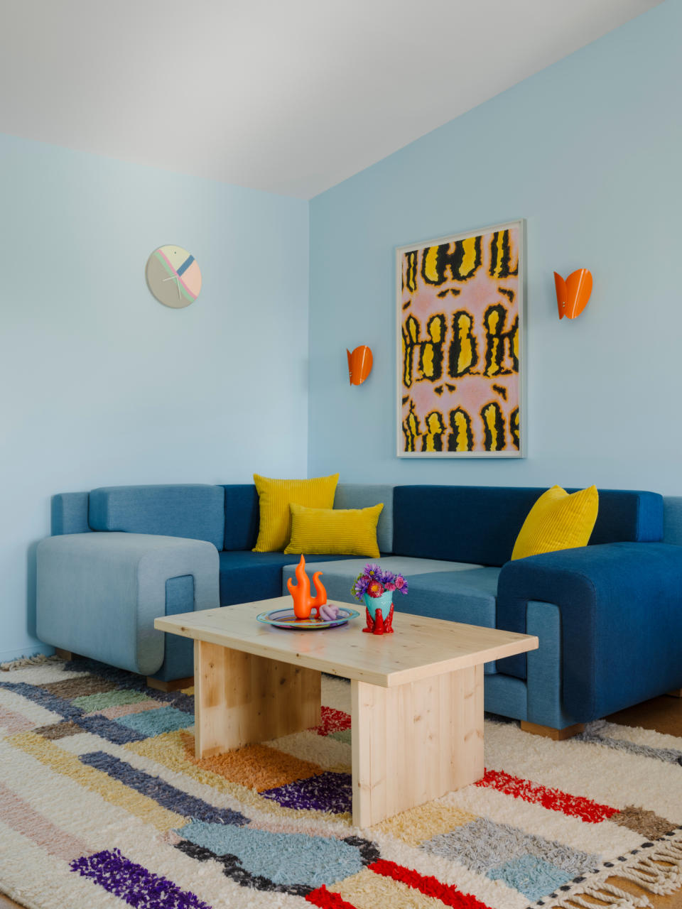 Tonal blue denim sofa against light blue wall with orange sconces and yellow artwork