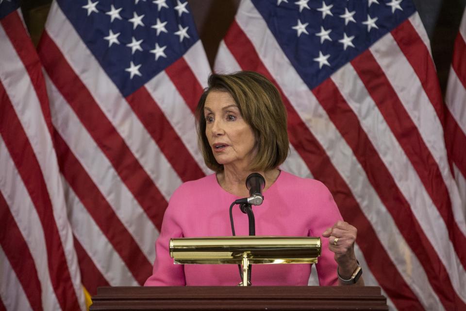 Democratic House Speaker Nancy Pelosi at a lectern in front of American flags.