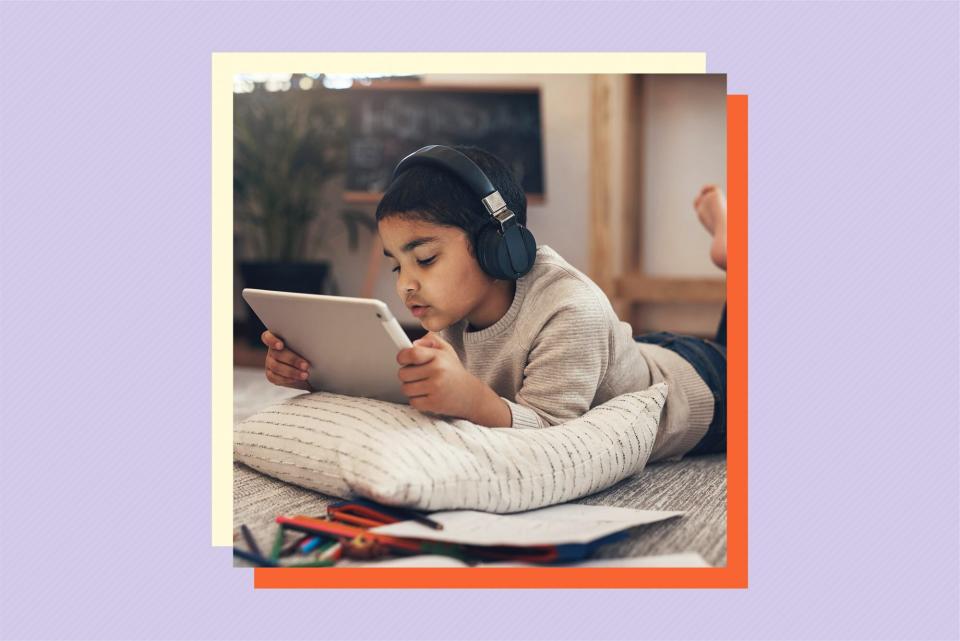 child lying on floor while using tablet and wearing headphones