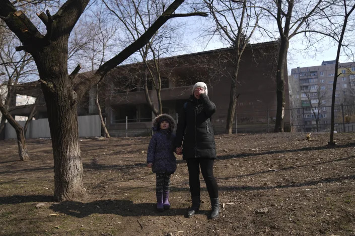 FILE - A woman reacts as she stands with her daughter as she waits for her husband to flee a burning apartment in Mariupol, Ukraine, March 13, 2022. Since March 1, the Russian military has pummeled Mariupol with fierce artillery barrages and air raids that have flattened most of what once was a bustling seaside city. (AP Photo/Evgeniy Maloletka, File)