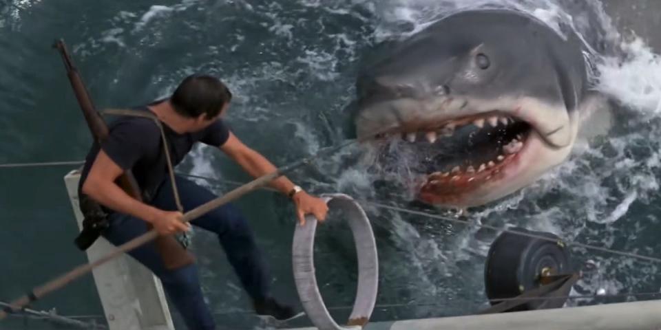The protagonist of the film stands above the animatronic shark with a spear.