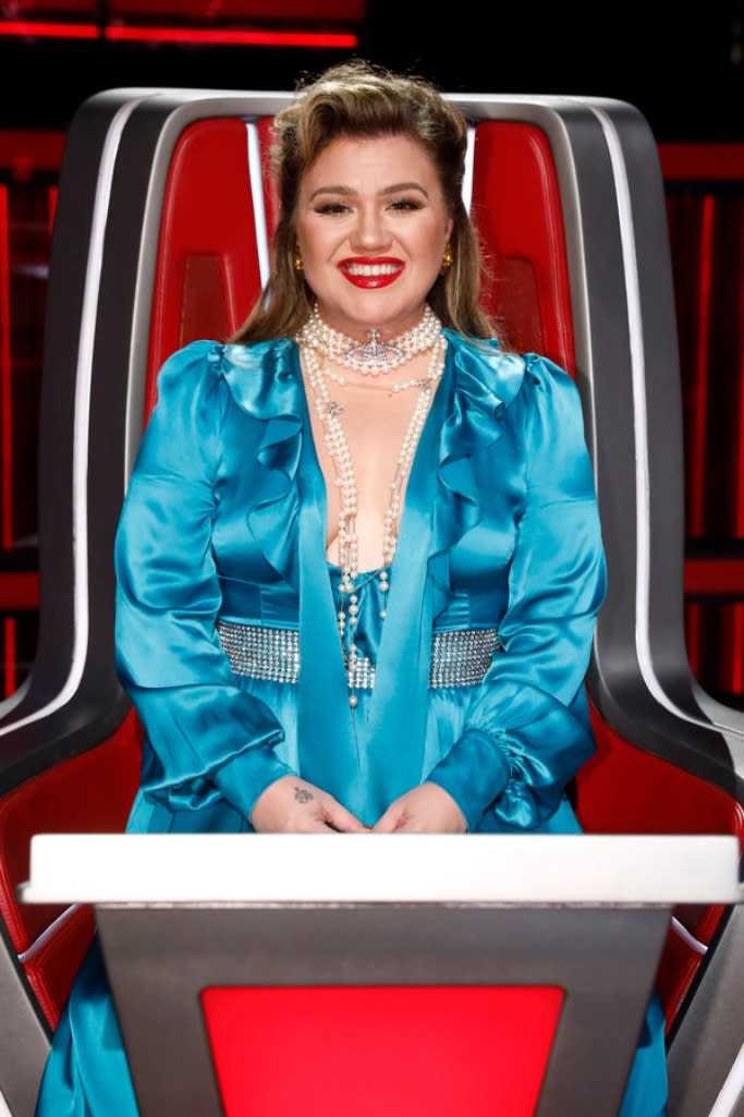 Kelly Clarkson shows off a vibrant blue satin gown featuring a crystal-embellished waist and draped pearls around her neck. - Credit: NBC