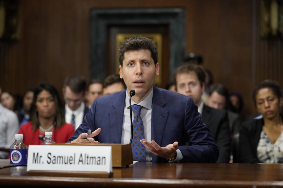 OpenAI CEO Sam Altman at the microphone, with other attendees arrayed behind him.