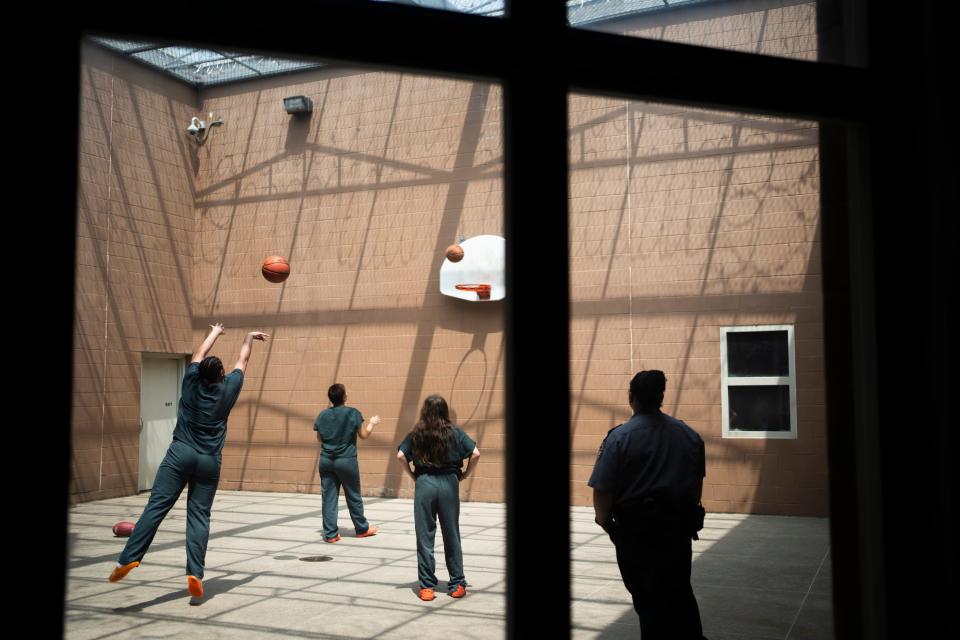 Three teenage girls shoot hoops in the barbed wire enclosed courtyard at Multi-County Juvenile Detention Center in Lancaster while a guard stands watch.