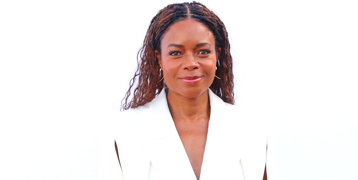 naomie harris, a woman stands looking at the camera smiling, she has curly brown hair and wears a white suit