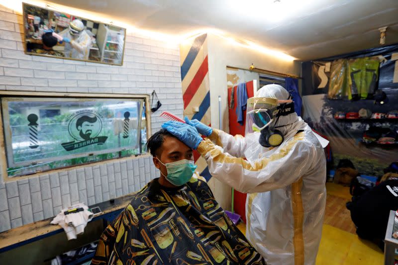 Herman Maulanasyah, a 40-year-old hair stylist, gives a haircut to a customer at his barbershop, while wearing a handmade protective suit in a tribute to the country's medical workers tackling the coronavirus disease (COVID-19) in Bogor