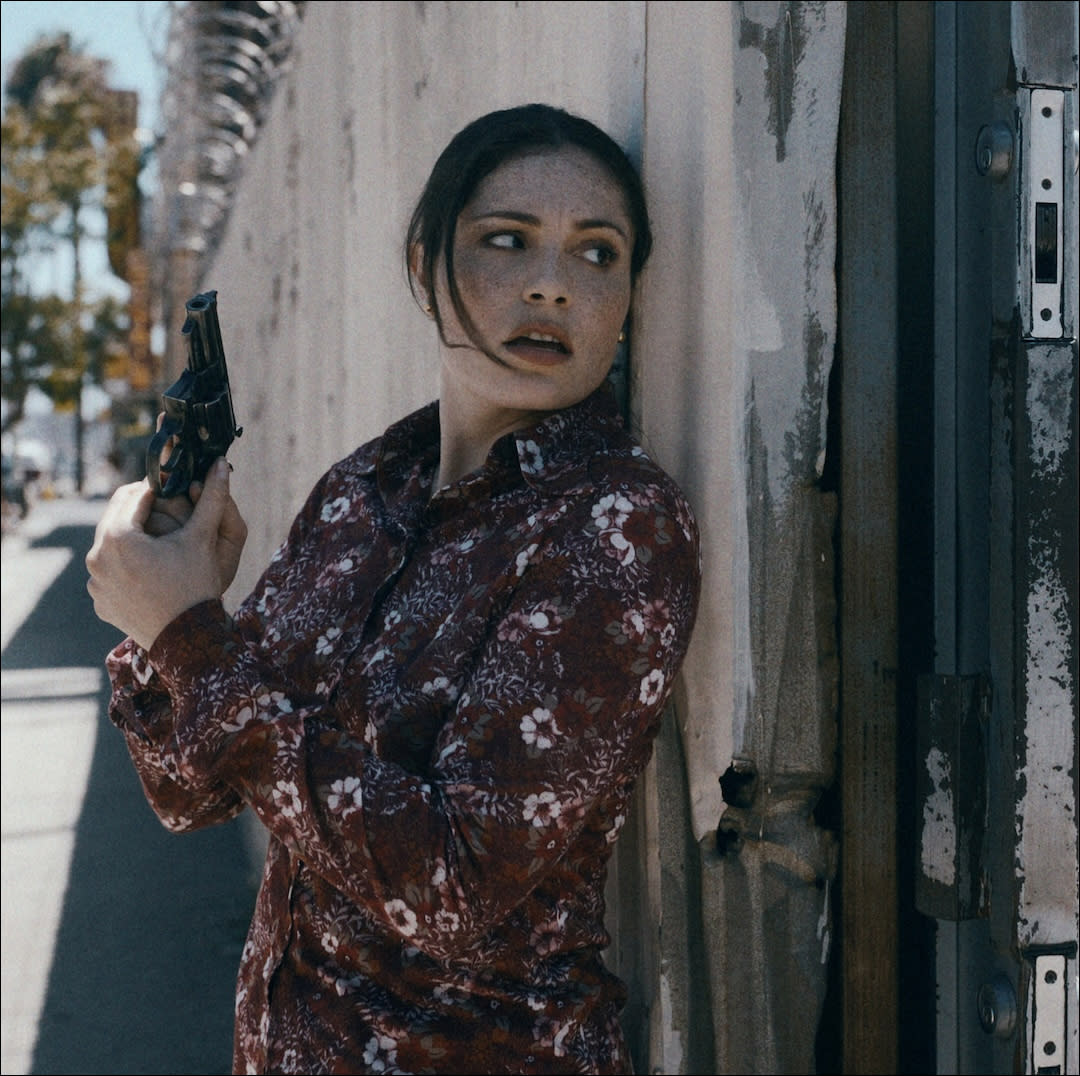  A woman (Juliana Aidén Martinez as June Hawkins) hides behind a wall while holding a gun. 
