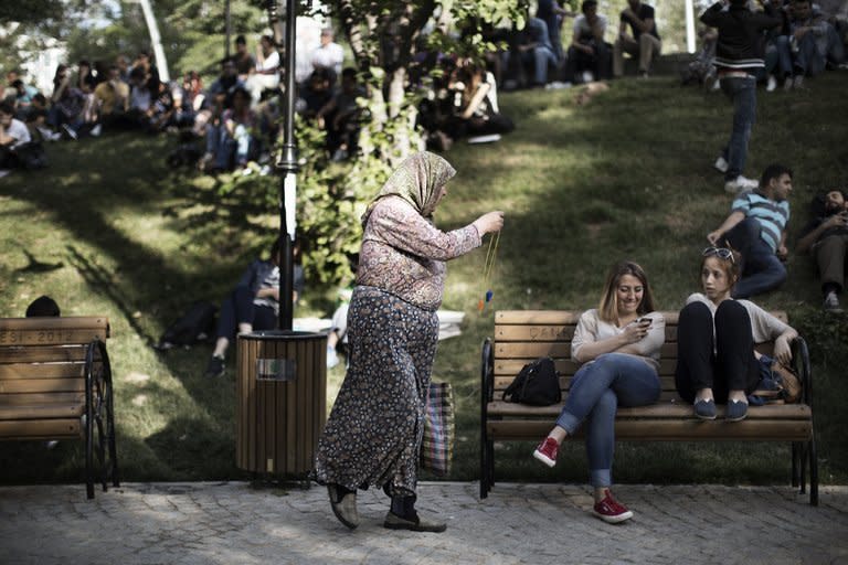 A traditionally-veiled Turkish woman sells whistles to young activists sitting at Kugulu Park in Ankara on June 7, 2013. Hotel reservations may be down after a week of violent mass protests in Turkey, but plucky tourists on the ground have taken the unrest in their stride