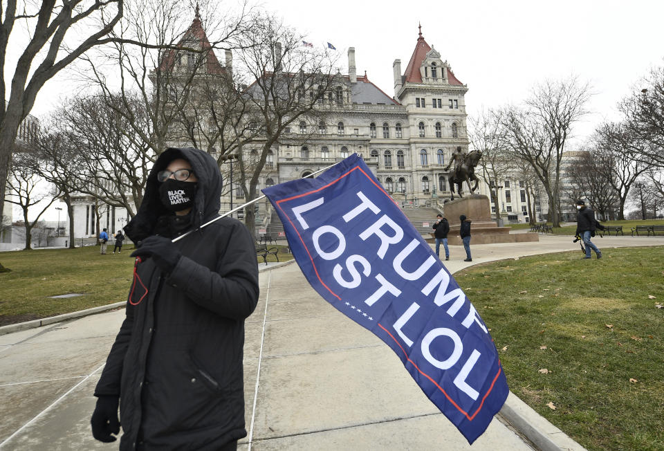 Christina Janowitz of Guilderland, N.Y., from the group "All Of Us' holds a flag while counter-protesting a Trump rally ahead of the inauguration of President-elect Joe Biden and Vice President-elect Kamala Harris at the New York State Capitol Sunday, Jan. 17, 2021, in Albany, N.Y. (AP Photo/Hans Pennink)