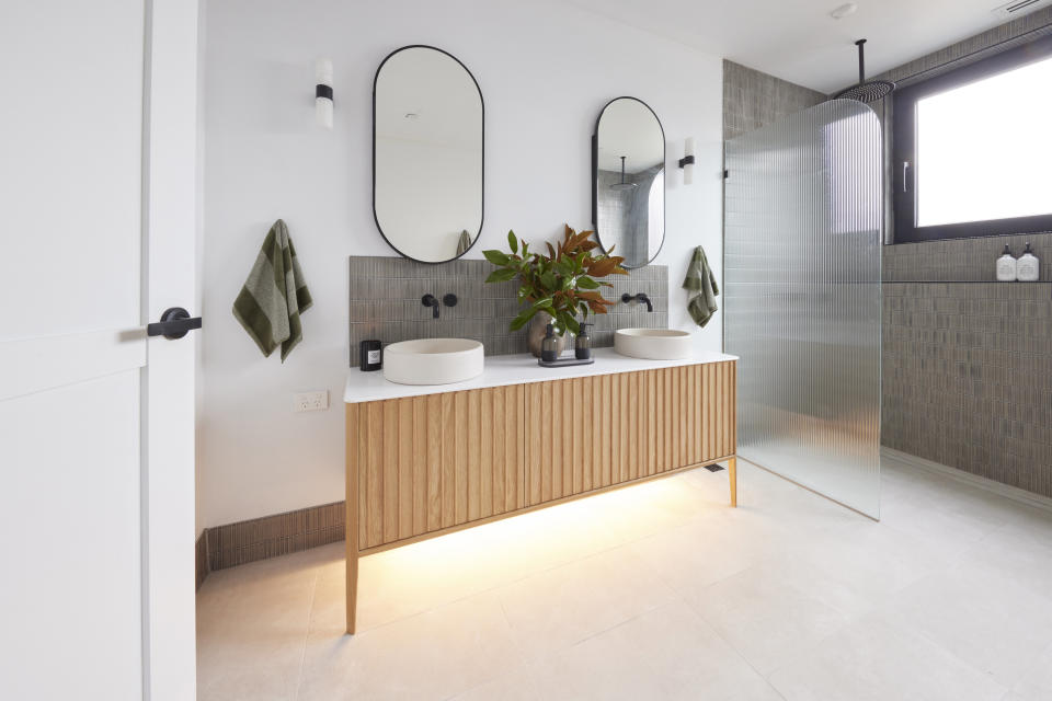 A shot of the vanity with wooden cupboards, two mirrors and the shower or the right. 