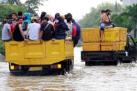 Workers sit on trucks driving through a road flooded at an area affected by land subsidence and rising sea levels in North Jakarta