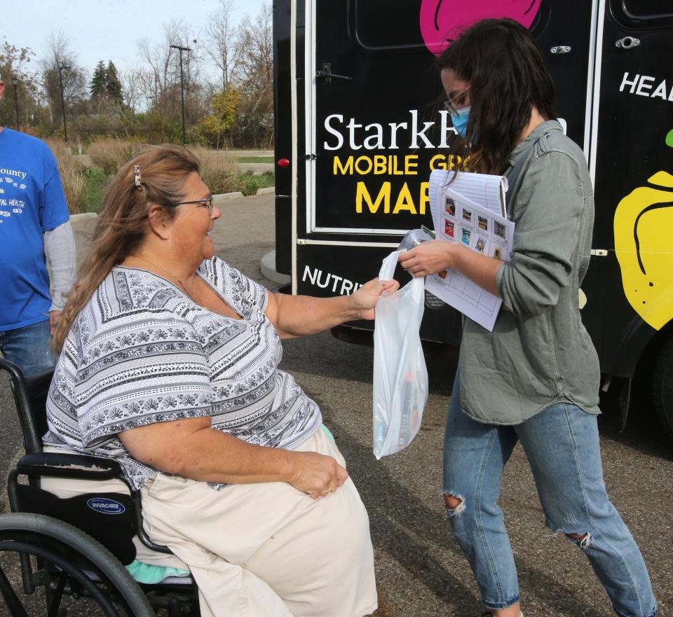 Stephanie Huberty is handed items from Azella Markgraf, StarkFresh's mobile grocery market coordinator, at the Wellness Village at Midway - one of the eight weekly stops that StarkFresh will continue to visit through winter.