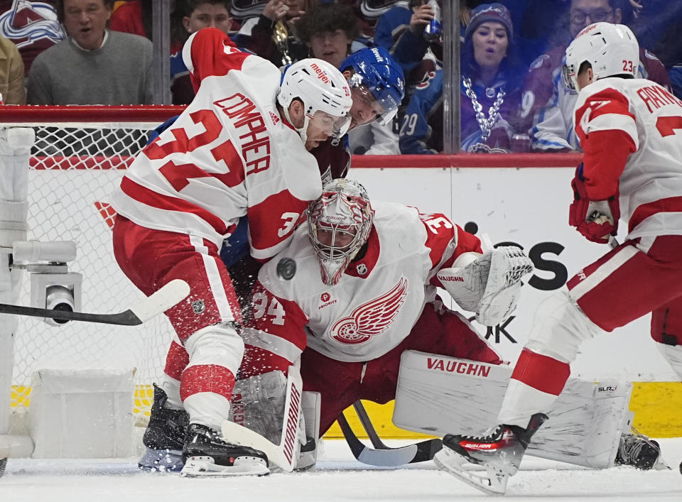 Detroit Red Wings goaltender Alex Lyon stops a shot as left wing J.T. Compher, front left, defends against Colorado Avalanche right wing Mikko Rantanen during the second period of an NHL hockey game Wednesday, March 6, 2024, in Denver. (AP Photo/David Zalubowski)