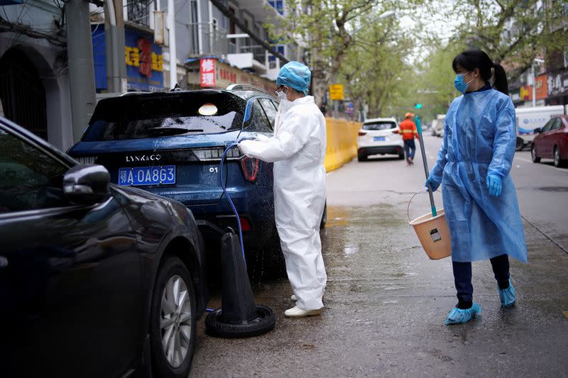 A woman wearing a protective suit washes a car on a street in Wuhan