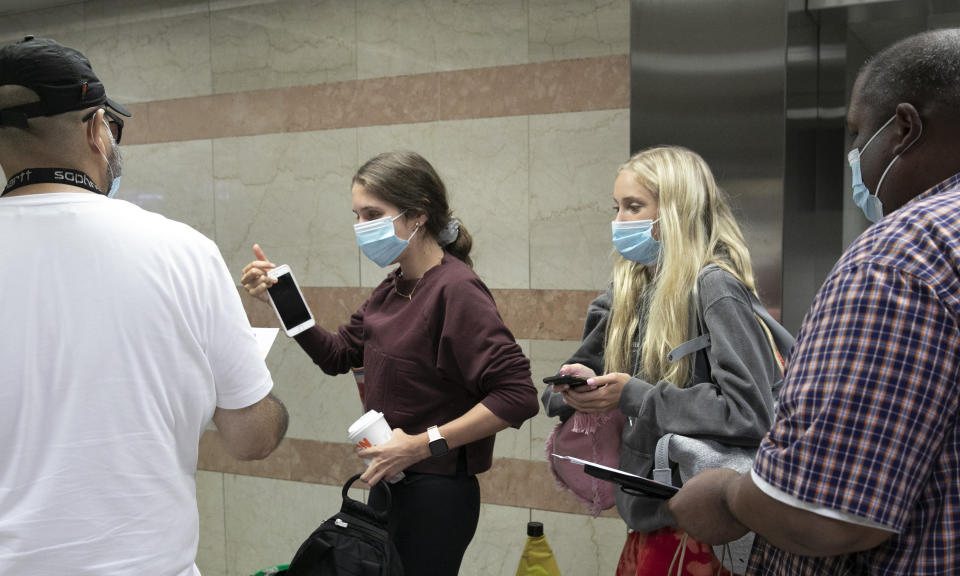 Travelers, center, get information leaflets from employees with the Mayor's Office of Public Engagement as they arrive at Amtrak's Penn Station, Thursday, Aug. 6, 2020, in New York. Mayor de Blasio is asking travelers from 34 states and Puerto Rico, where COVID-19 infection rates are high, to quarantine for 14 days after arriving in the city. (AP Photo/Mark Lennihan)