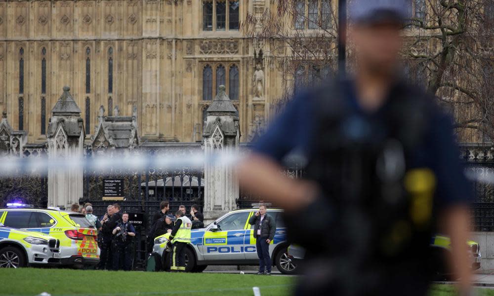Armed police officer stands guard as emergency services gather at Carriage Gates entrance of UK parliament