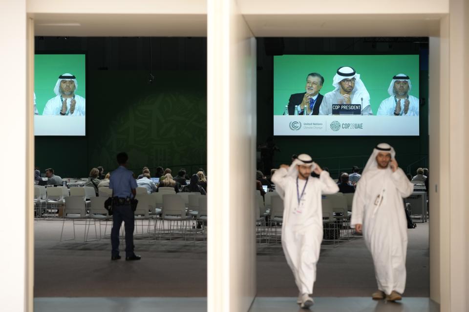 People walk out as COP28 CEO Adnan Amin, left, COP28 President Sultan al-Jaber, center, and COP28 Director-General Ambassador Majid Al Suwaidi, clap onscreen during a plenary session at the COP28 U.N. Climate Summit, Wednesday, Dec. 13, 2023, in Dubai, United Arab Emirates. (AP Photo/Peter Dejong)
