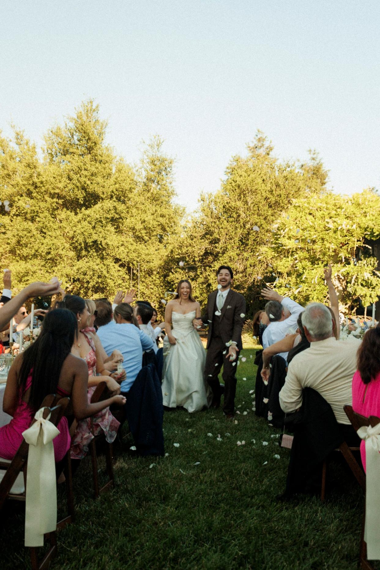 A bride and groom walk through their wedding reception as their guests throw flower petals around them.