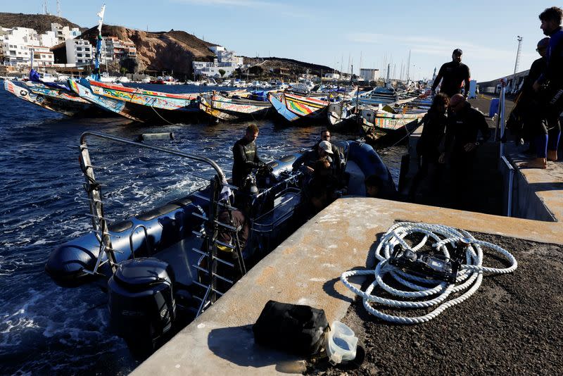 Tourists in diving gear prepare to leave on an inflatable boat near several abandoned wooden boats used by migrants in the port of La Restinga