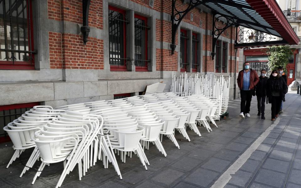 People walk past chairs and tables stacked on the closed terrace of a bar as the spread of the coronavirus disease  - Reuters