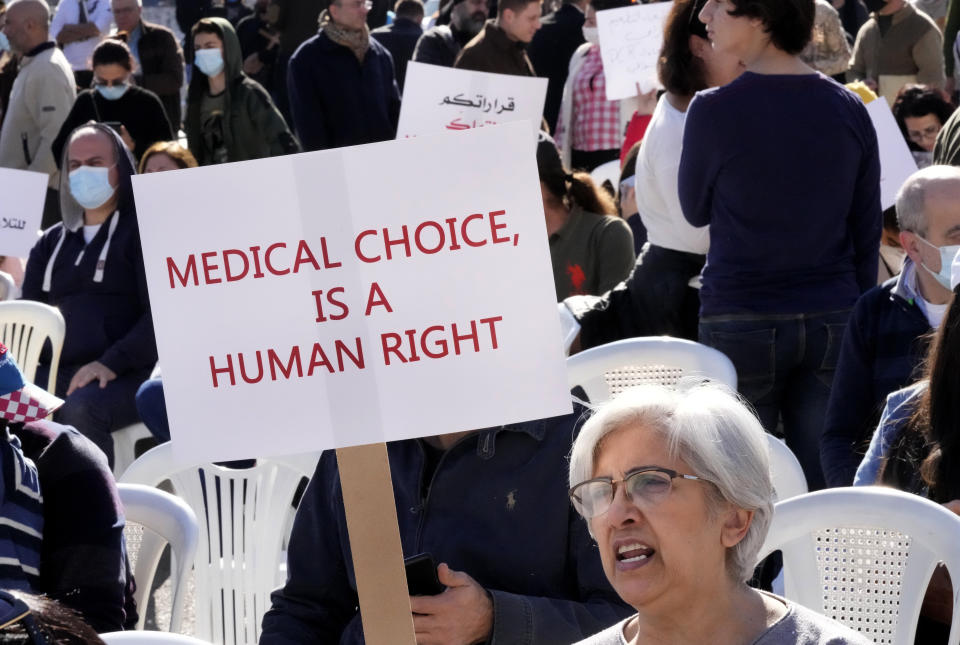 A protester shouts slogans as she holds a placard during a rally to protest measures imposed against people who are not vaccinated, in Beirut, Lebanon, Saturday, Jan. 8, 2022. Vaccination is not compulsory in Lebanon but in recent days authorities have become more strict in dealing with people who are not inoculated or don’t carry a negative PCR test. (AP Photo/Hussein Malla)