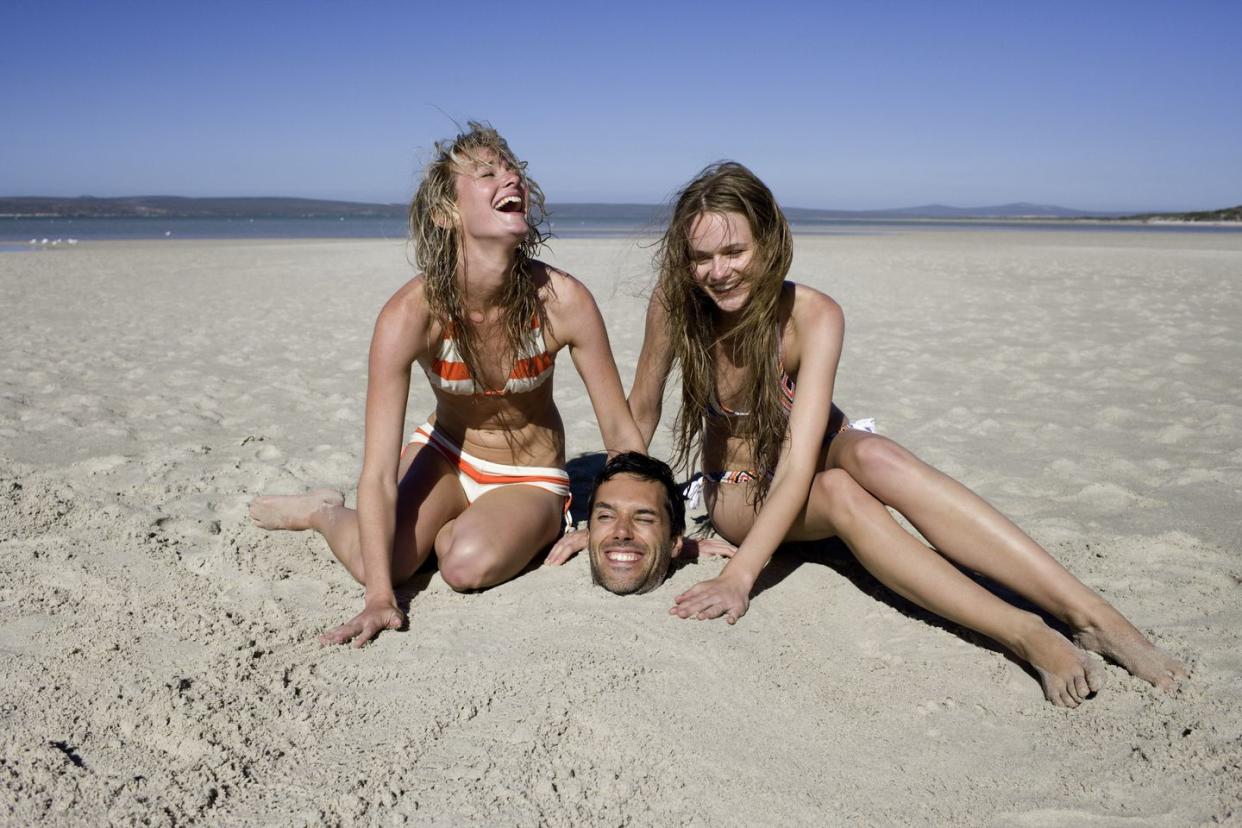young women burying man in sand laughing