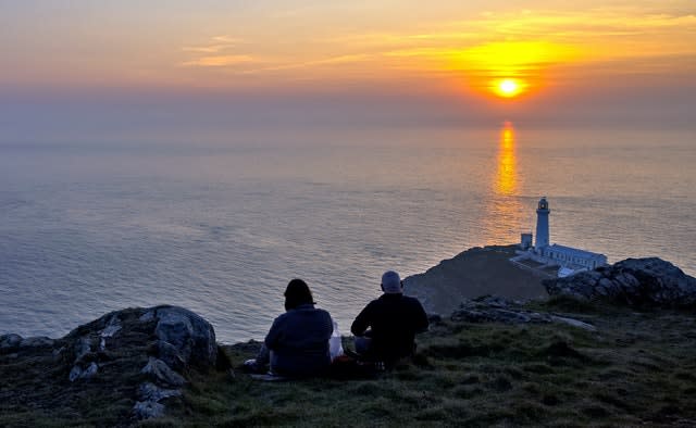 People watch the sun set behind South Stack lighthouse on Anglesey