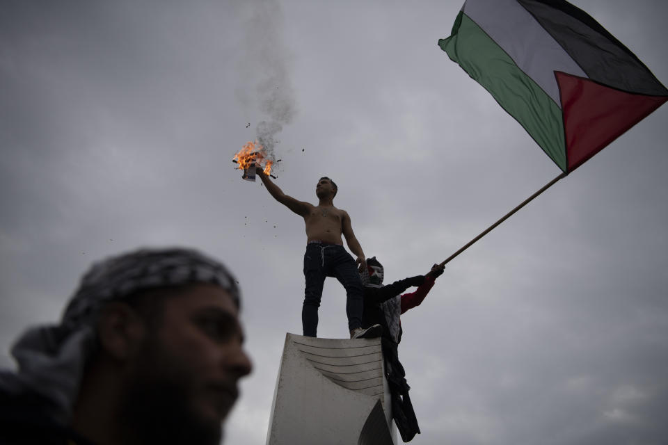 A man holds a burning Israeli flag, while another waves a Palestinian one, during a protest in front of the Israeli Embassy in Athens, Greece, Saturday, Jan. 27, 2024. Around 3,000 people staged a protest march early Saturday afternoon against the continuing Israeli military operations in Gaza. (AP Photo/Michael Varaklas)