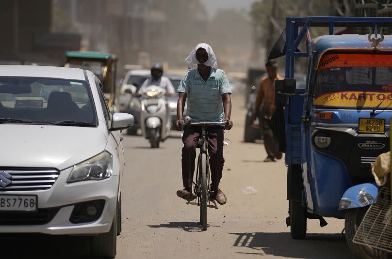 A man covers his face with cloth to protect from the heat as he rides a bicycle through a busy street in Jammu, India.