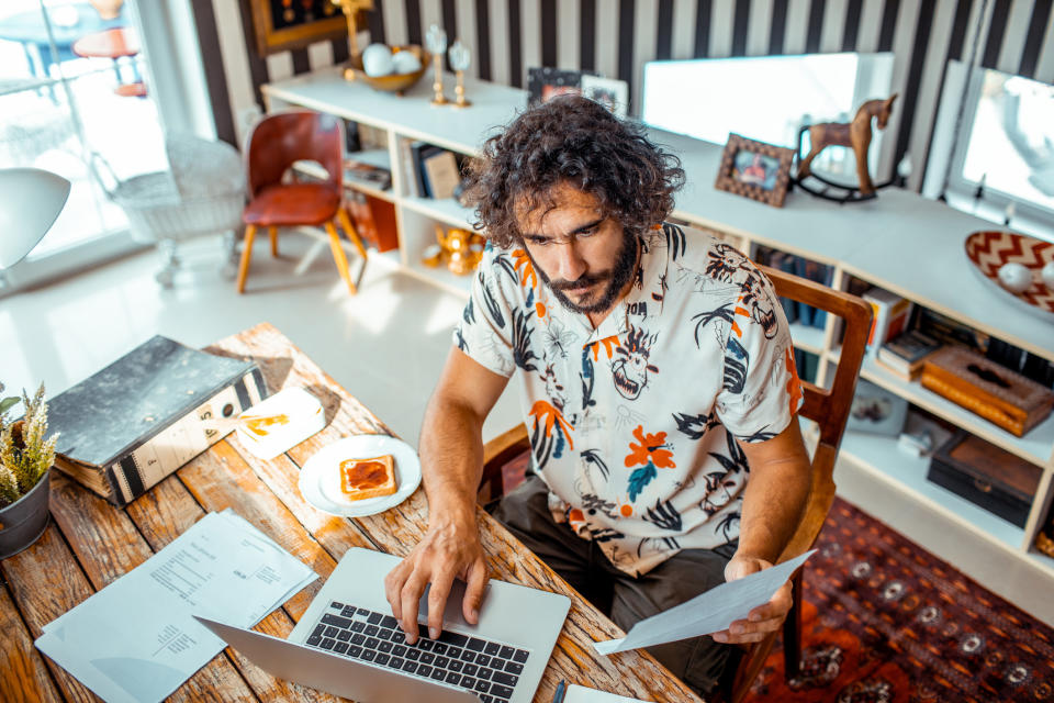 A man sitting at this laptop and looking at pieces of paper