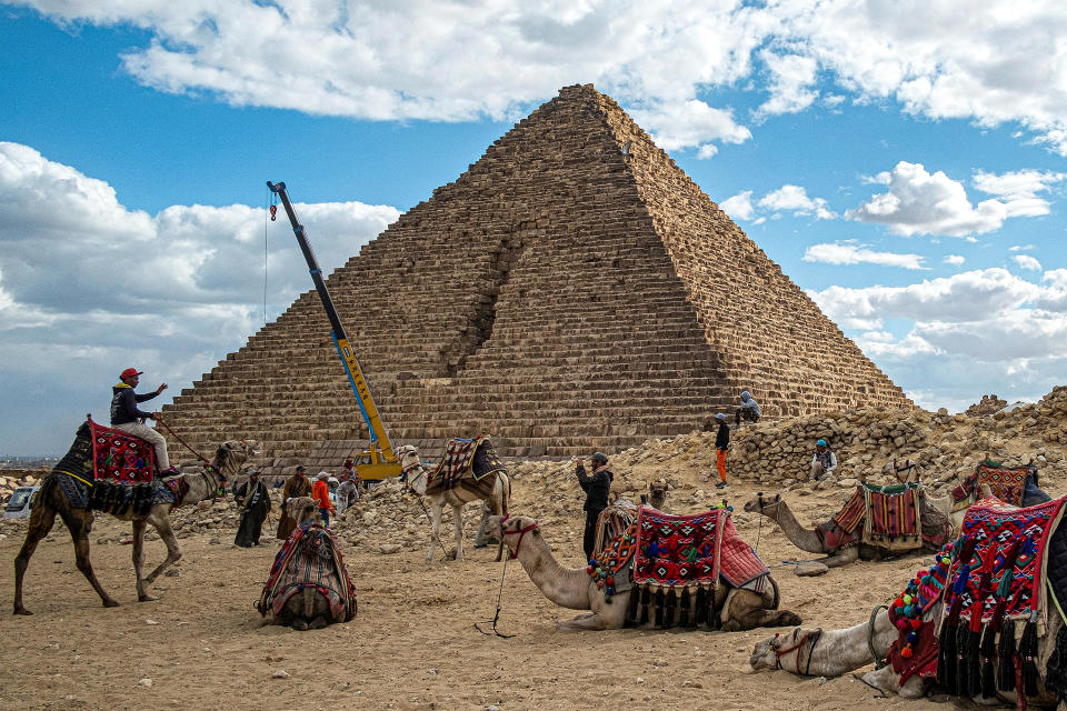 A crane lifting stones is pictured behind camels resting with their trainers by the Pyramid of Menkaure at the Giza Pyramids Necropolis, west of Cairo, Jan. 29, 2024. / Credit: KHALED DESOUKI/AFP/Getty