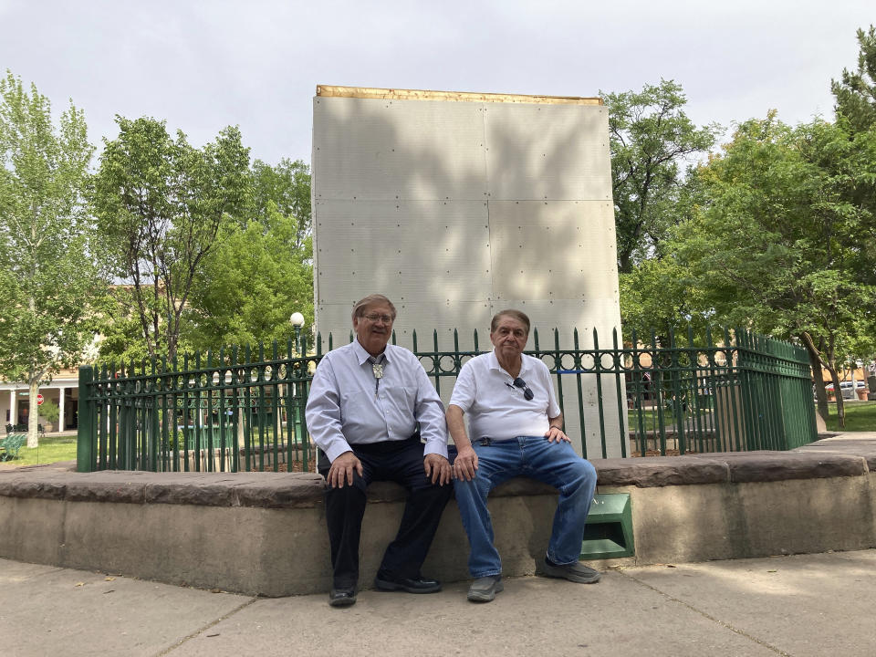 In this Monday, June 14, 2021, photo, Union Protectíva de Santa Fé president Virgil Vigil and vice president Richard Varela sit in front of the covered remnants of the Soldier's Memorial obelisk at the center of the Plaza in Santa Fe, N.M. Their Hispanic cultural association Union Protectíva de Santa Fé sued the city's mayor Wednesday, June 16, over the destruction of the obelisk by activists the year before, and plans to permanently move the memorial. The lawsuit argues that the obelisk, which honors Hispanic soldiers that fought and died for the Union in battles with Confederate soldiers and Indigenous tribes, is a protected historical site. (AP Photo/Cedar Attanasio)